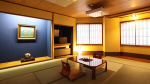 A traditional Japanese room with tatami flooring, a low wooden table, a cushioned bench, a shelf with items, and a framed picture on the wall. - Hotel Yamakawa (Yonezawa)