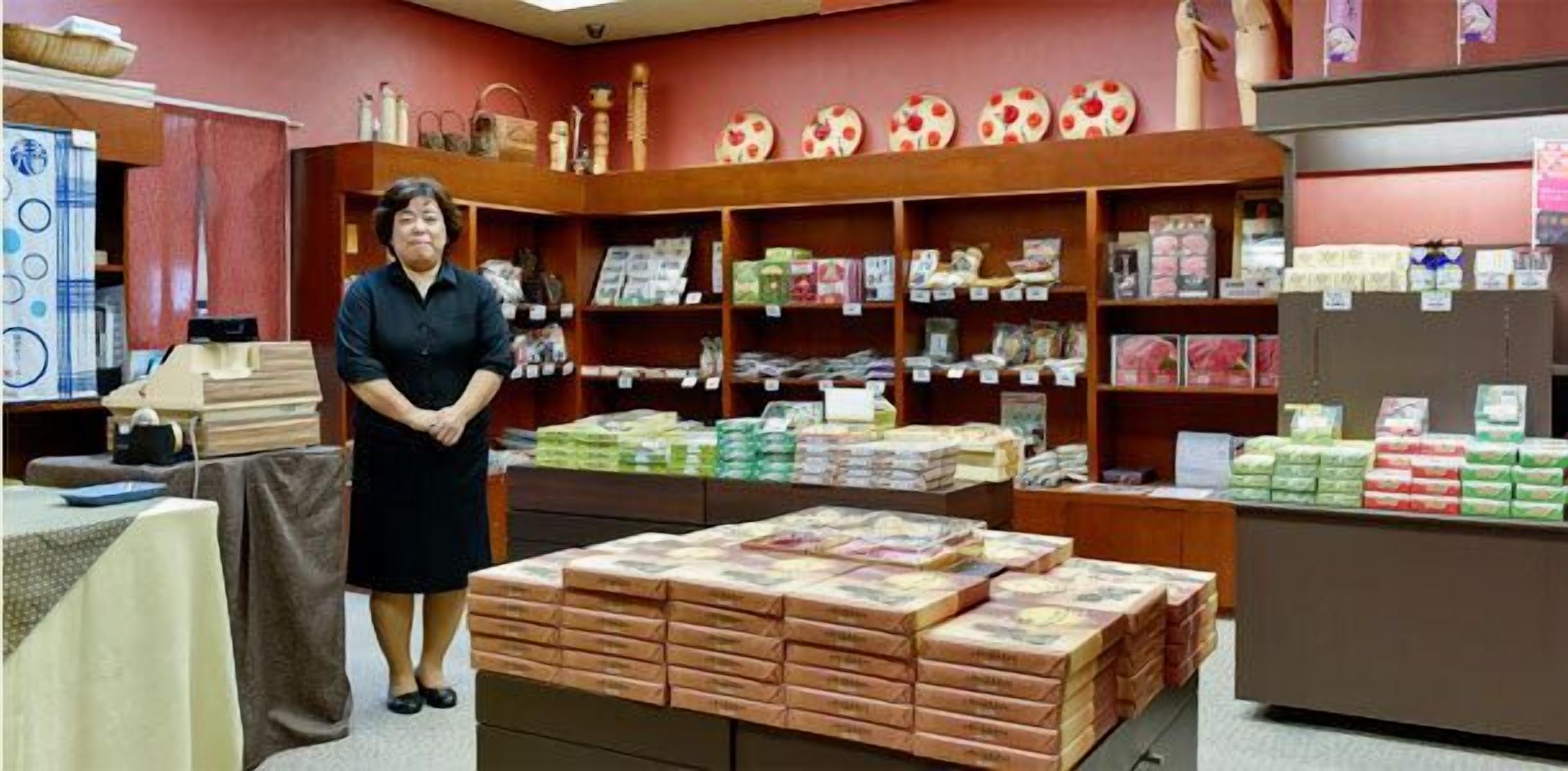 A room with a person standing in front of shelves stocked with various items, including books and boxes.