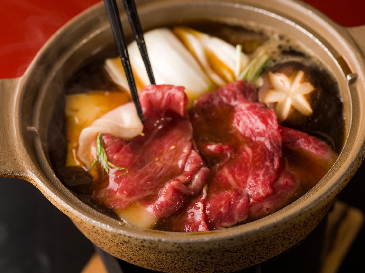 A bowl of hot pot with meat and vegetables.