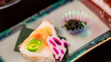 Un plat de sushis composé d’avocat vert coupé en tranches et de gingembre mariné rose, le tout présenté sur une assiette rectangulaire ornée d’un bord décoratif.
