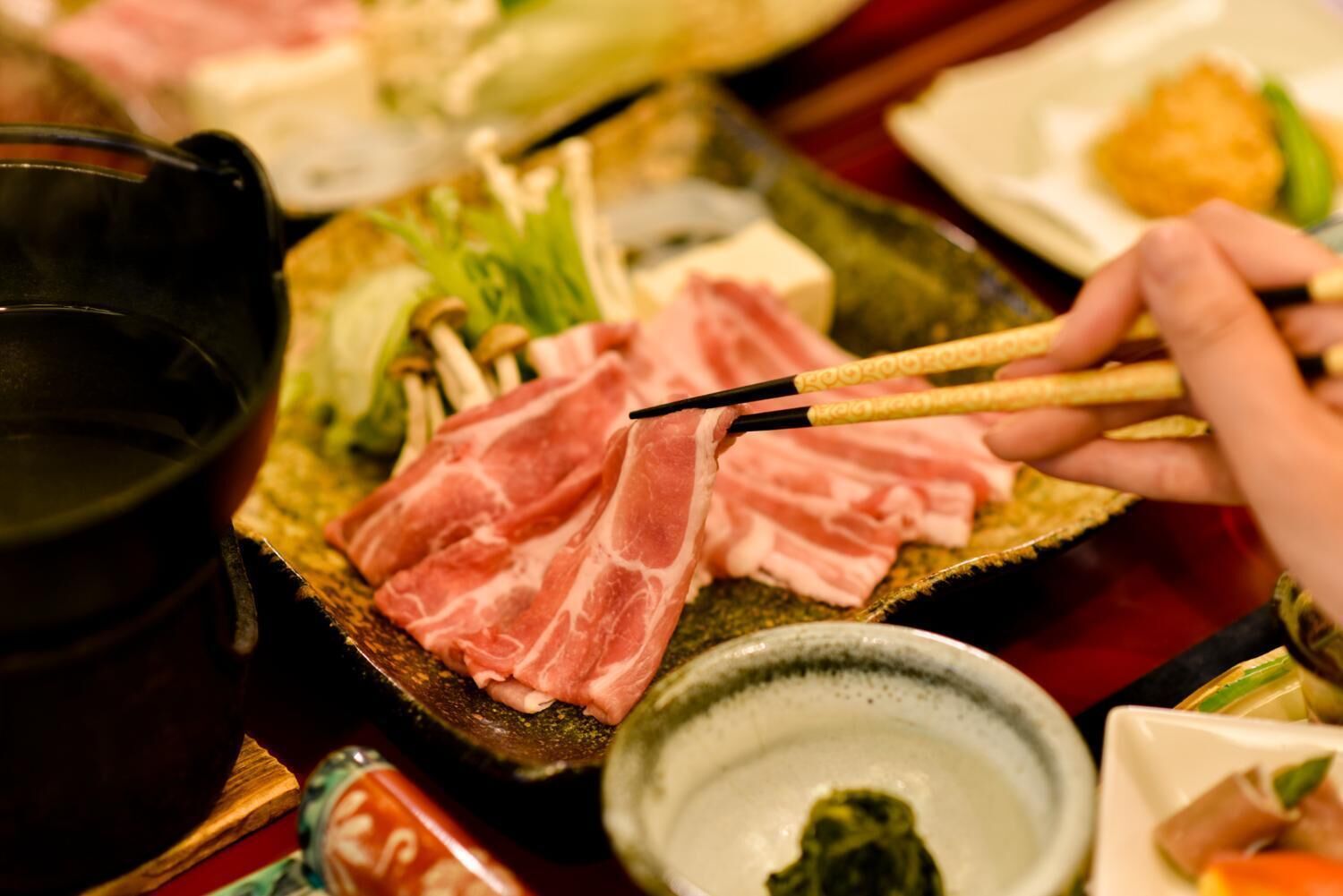 Un primo piano di un piatto di hot pot con diversi tipi di carne e verdure, una ciotola di zuppa e bacchette.