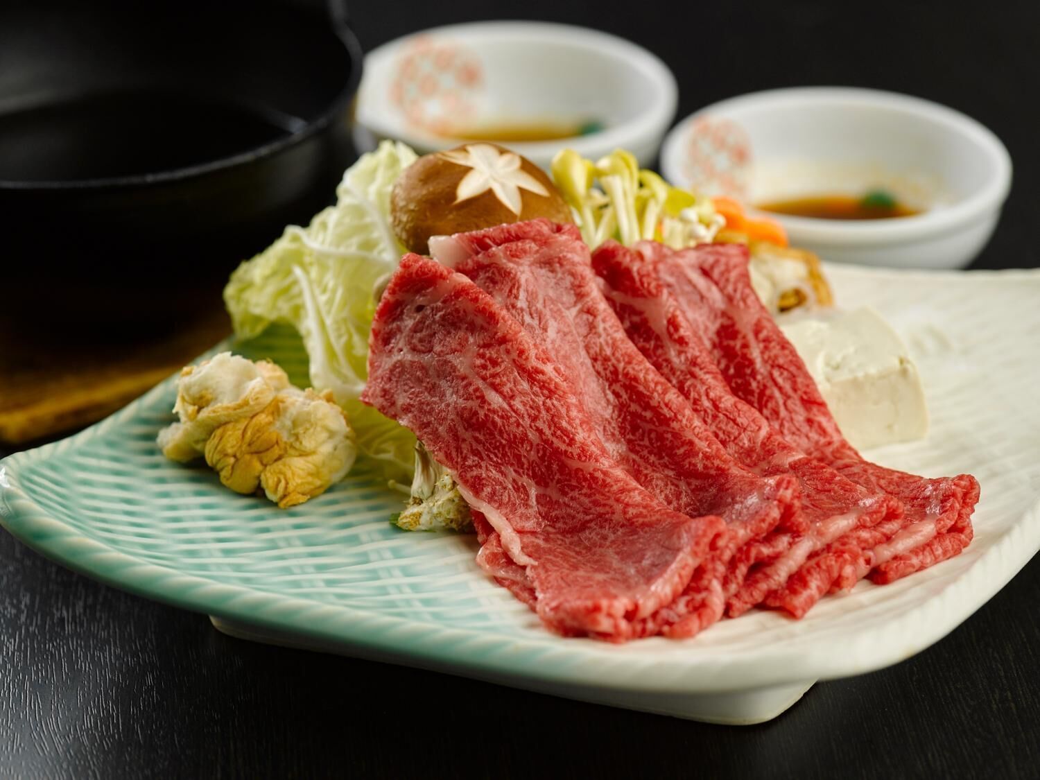 A plate with raw beef, vegetables, and a small bowl of sauce.