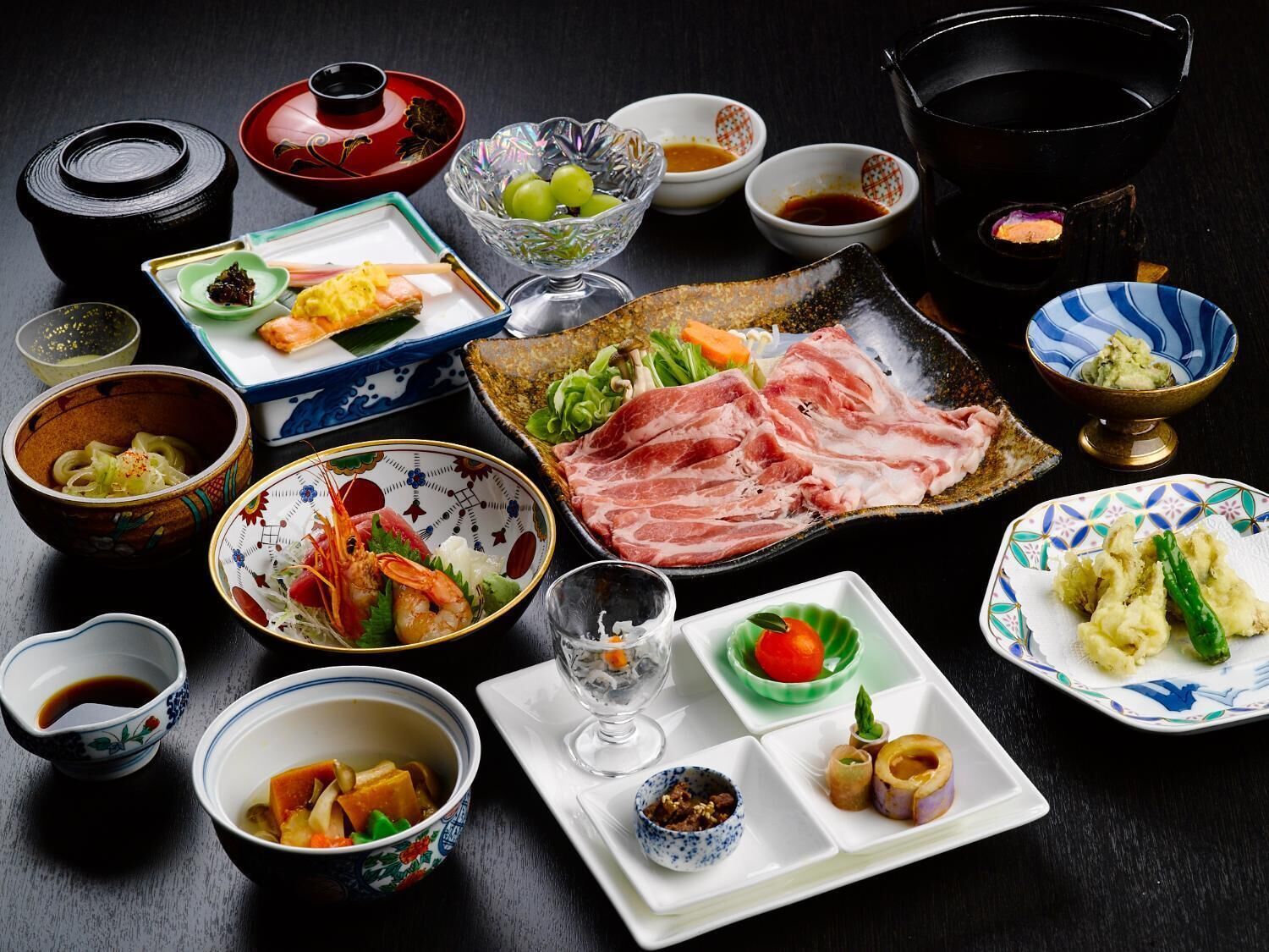 Variedad de platos japoneses sobre una mesa, incluyendo sashimi, sushi y otros alimentos tradicionales, acompañados de pequeños recipientes con salsas y condimentos.