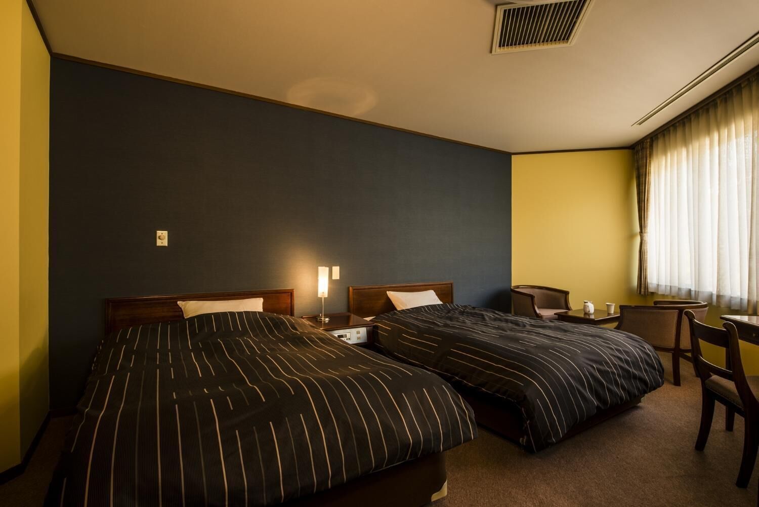 Quarto de hotel com duas camas, uma escrivaninha e uma cadeira.