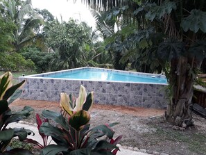 A rectangular swimming pool with a stone wall surrounding it, set in a garden with various plants and trees. - The Green Valley Inn (Unitedville)