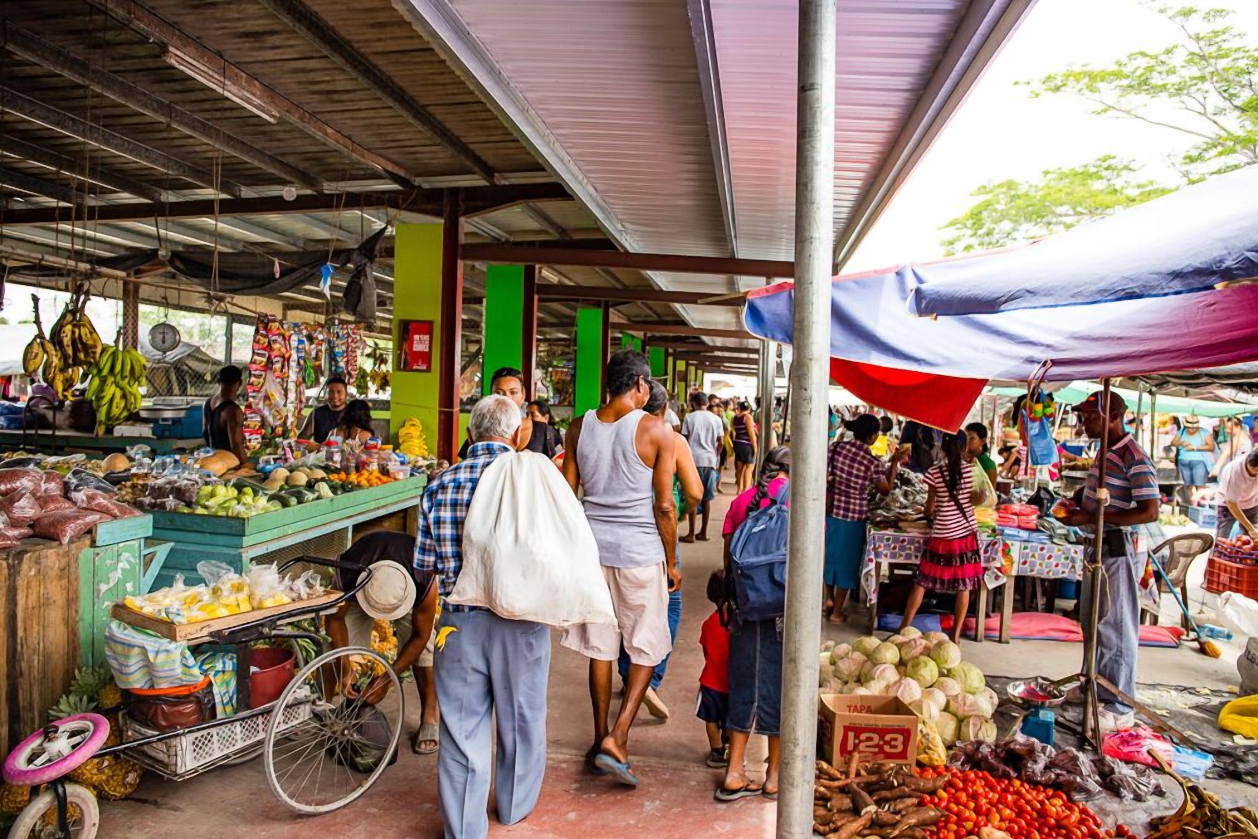 Un marché animé en plein air, avec de nombreux étals proposant des fruits, des légumes et d’autres produits.