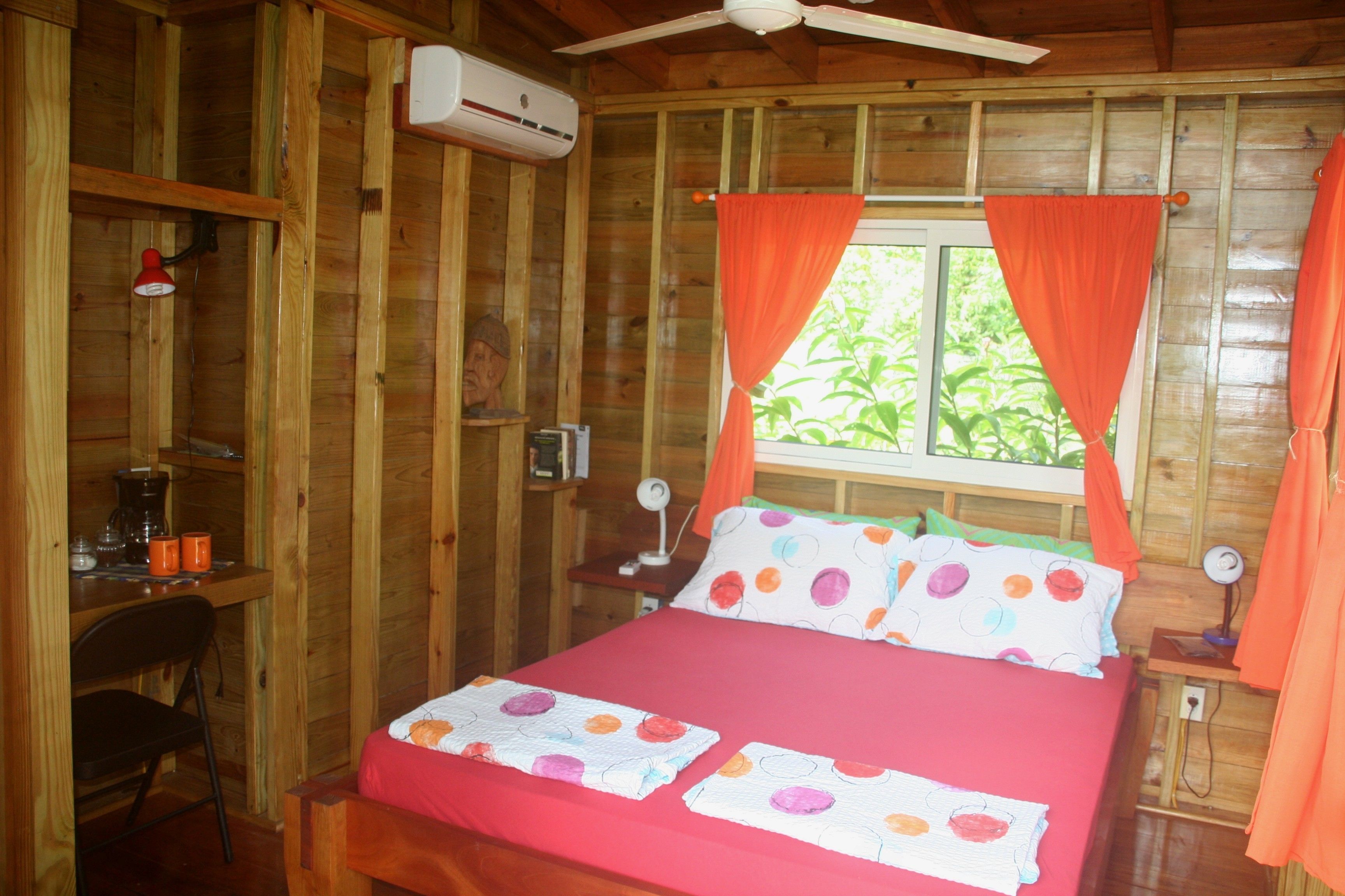 A wooden cabin room with a bed, a desk, and a chair.