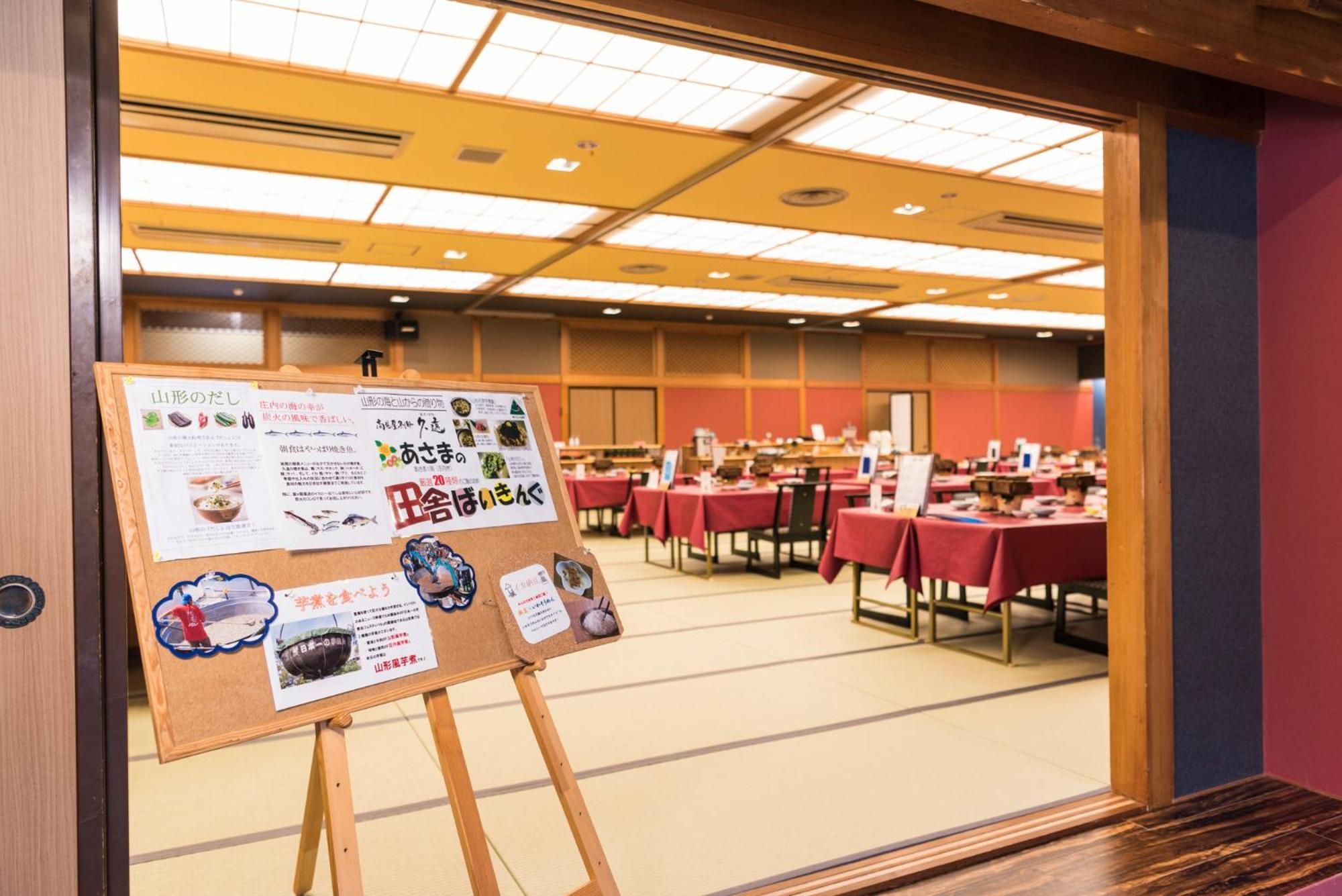 Un salón de conferencias con mesas, un tablón de anuncios con carteles informativos y un techo con luces fluorescentes.
