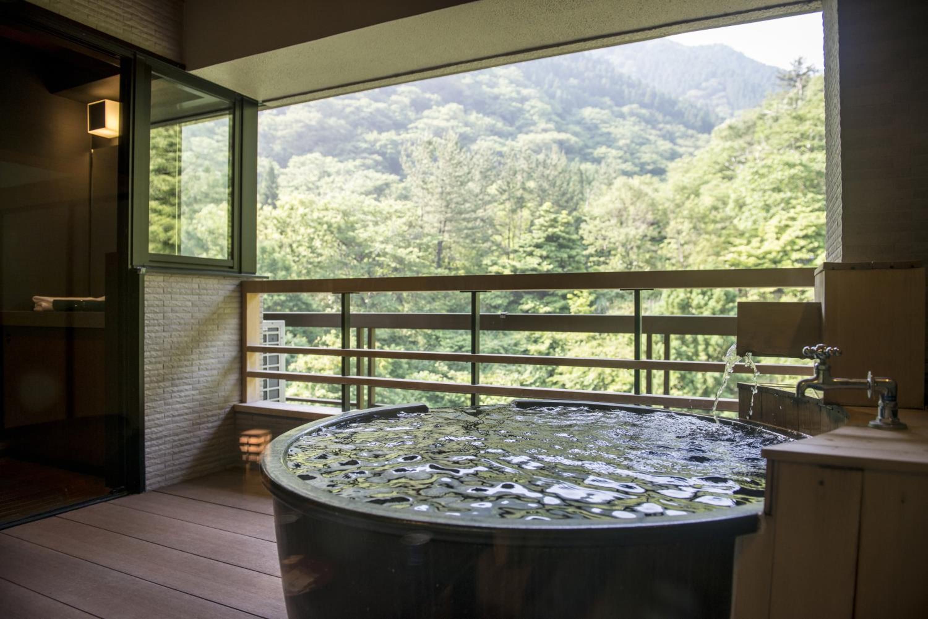 A bathroom with a large bathtub, a window with a view of a forest, and a wooden deck.