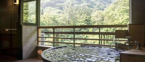 A bathroom with a large bathtub, a window with a view of a forest, and a wooden deck.