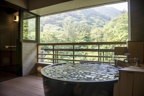 Un baño con una bañera grande, una ventana con vistas a un bosque y una terraza de madera.