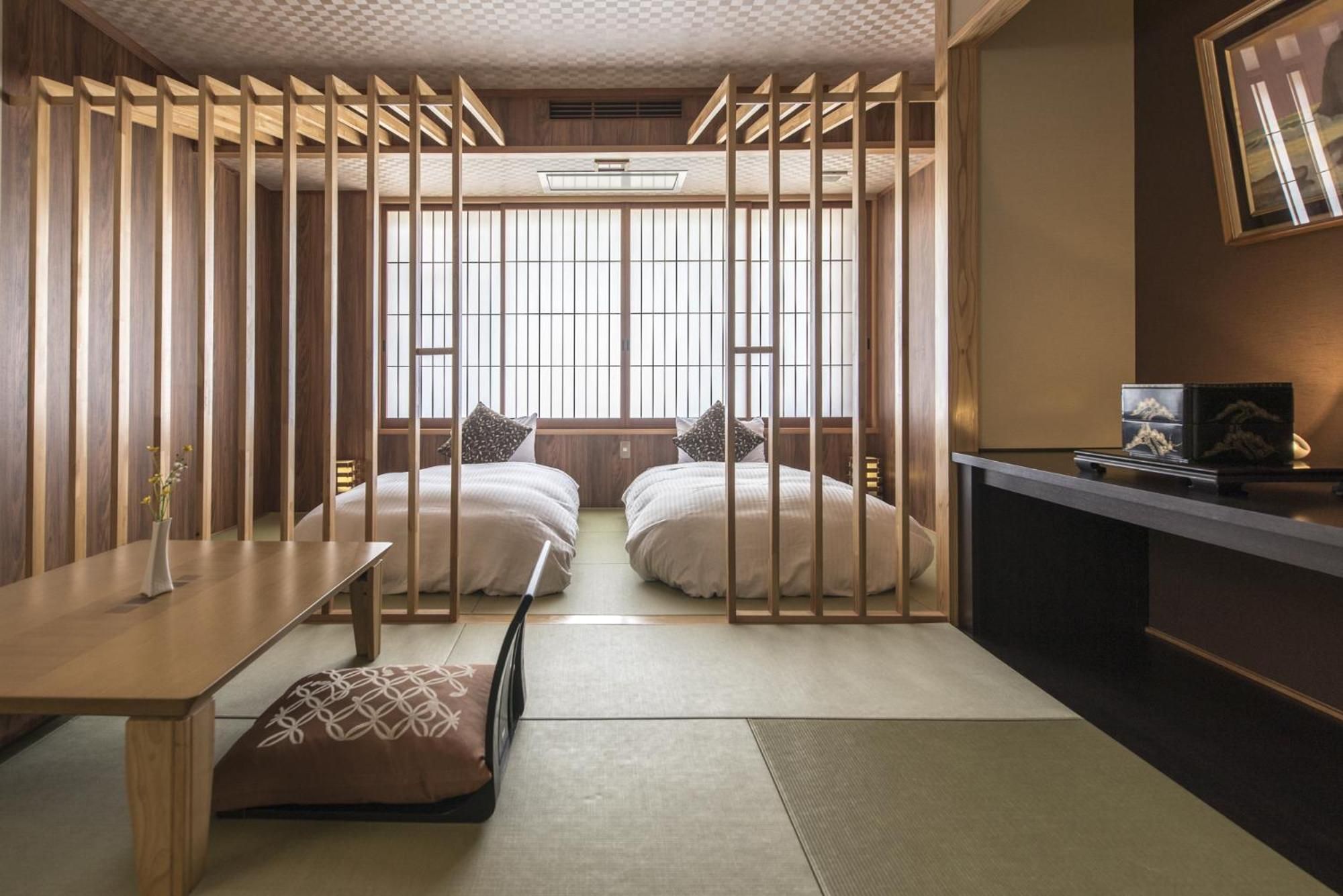 A traditional Japanese-style room with tatami flooring, a low table, two beds with pillows, and a sliding door.