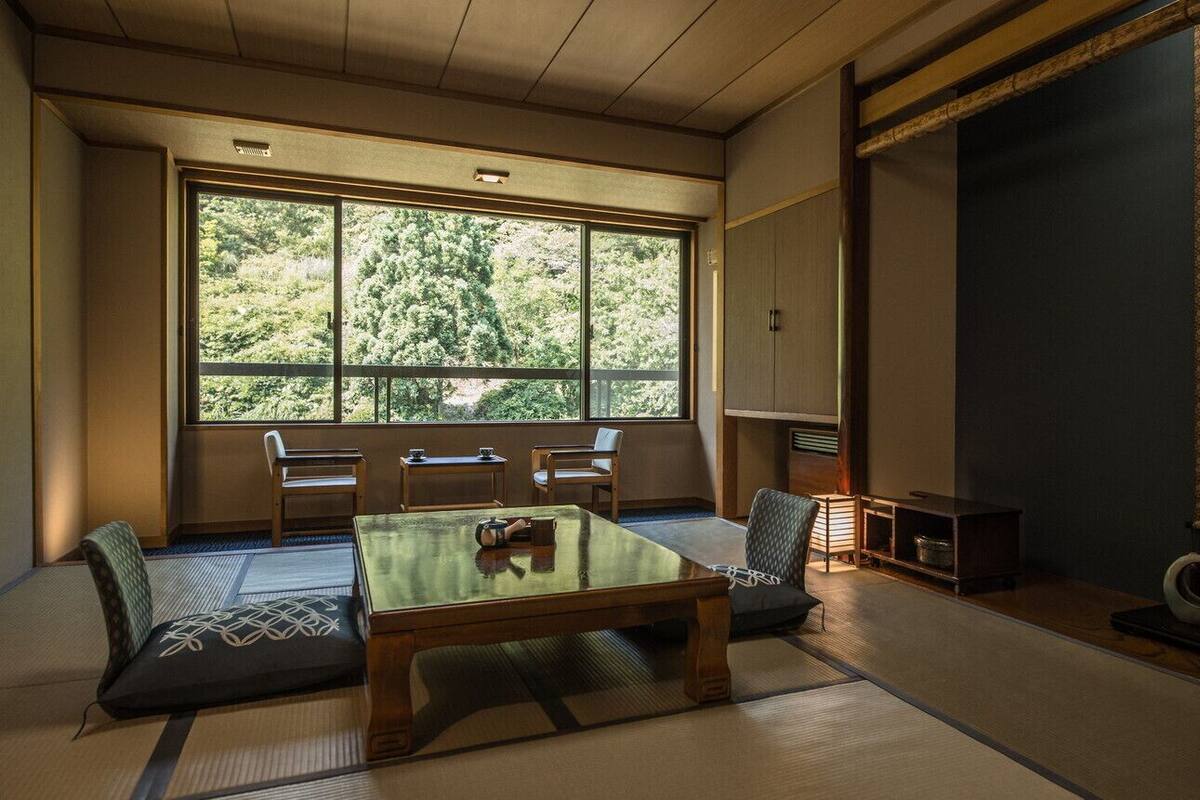 Um quarto japonês tradicional com tatames, uma mesa baixa e uma grande janela.