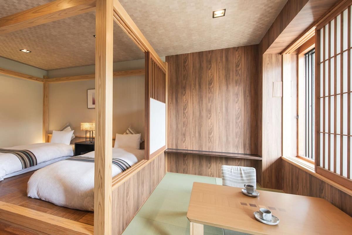 Um quarto em estilo japonês tradicional, com chão de esteira de tatame, uma mesa baixa com uma xícara e uma cama com cabeceira de madeira.