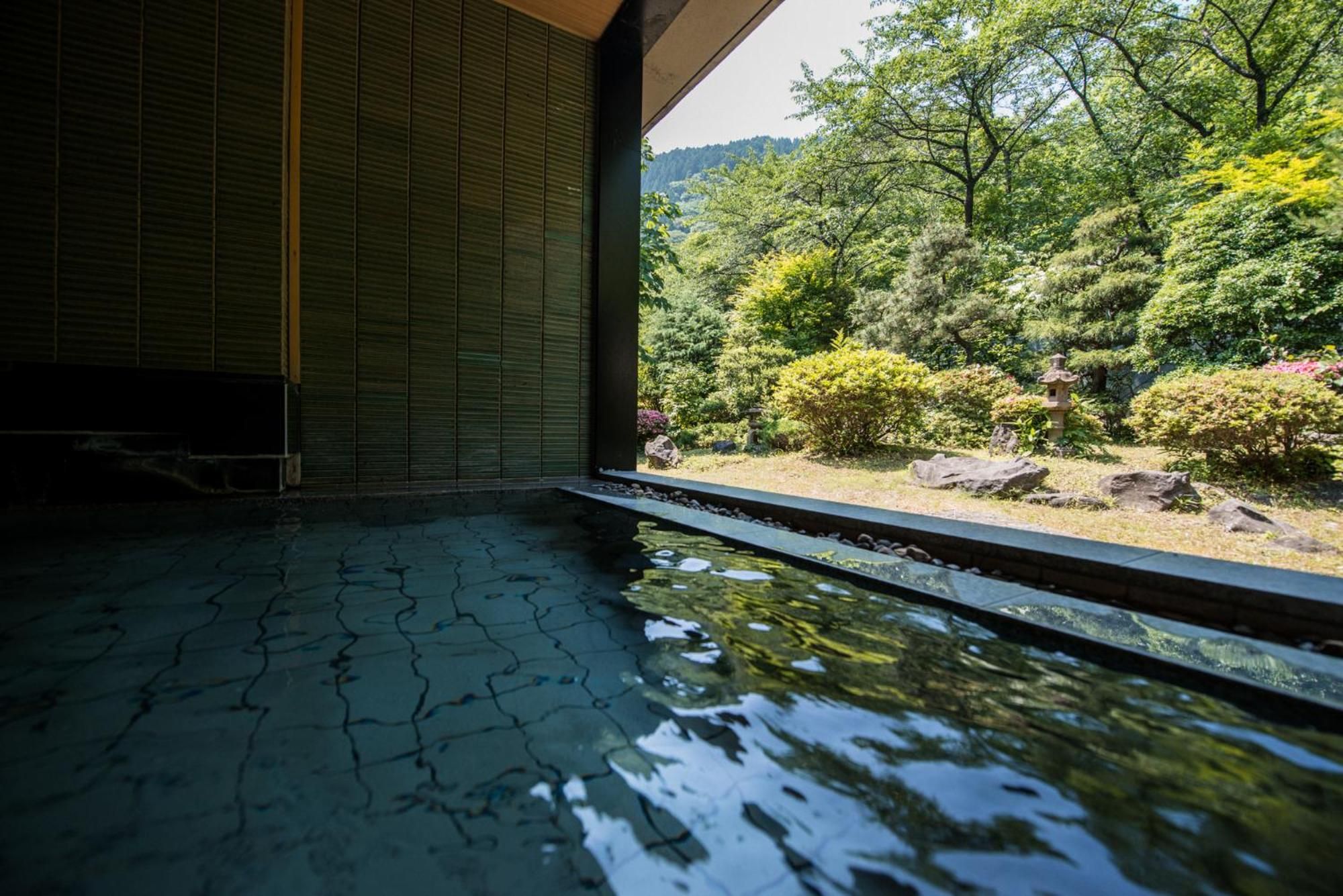 A traditional Japanese room with tatami flooring, a view of a lush garden, and a stone lantern.