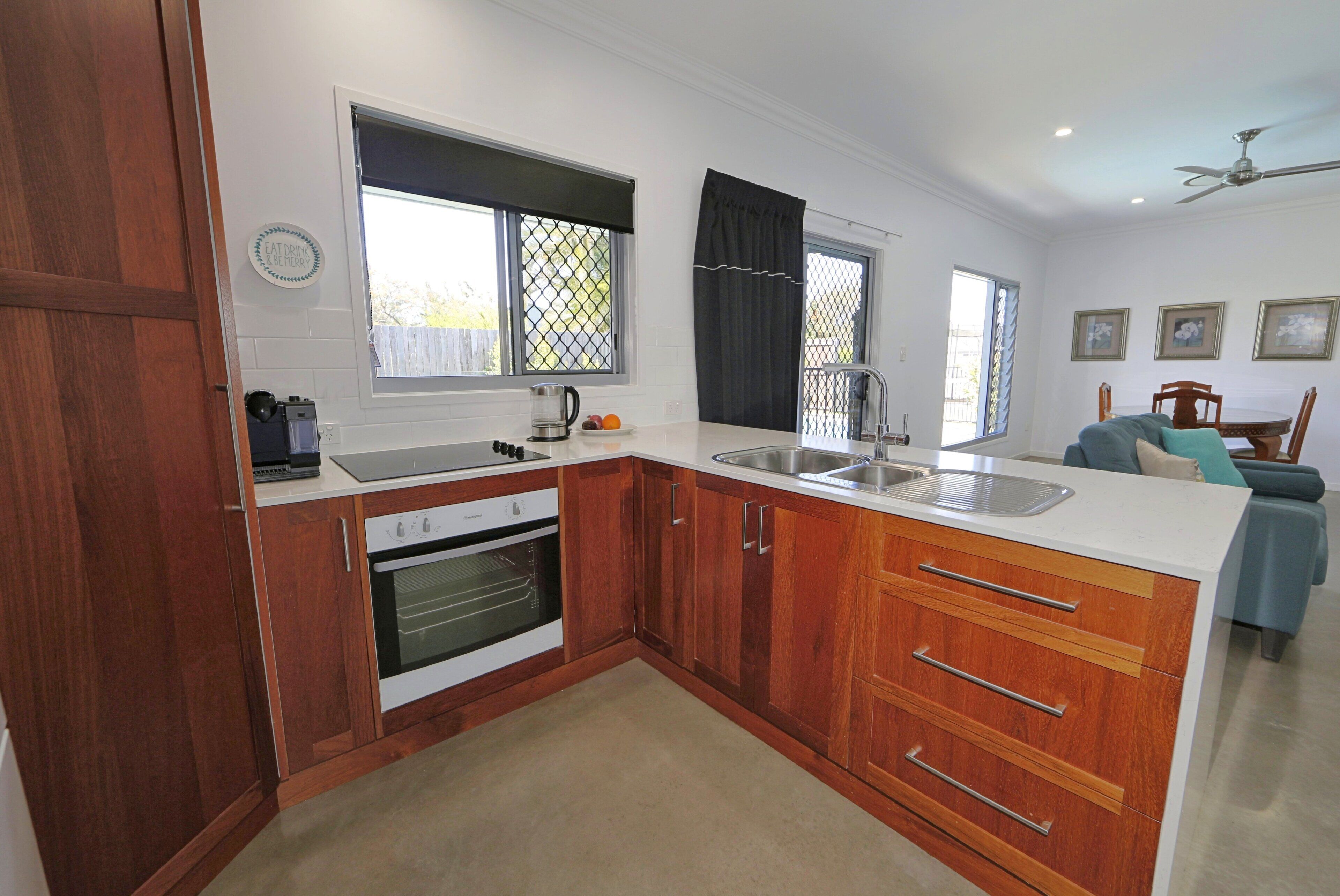 A modern kitchen with wooden cabinets, a built-in oven, a sink, and a dining area with a table and chairs.