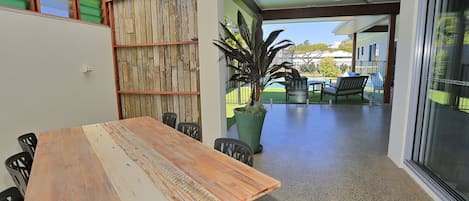 A wooden table with chairs, a potted plant, and a view of a pool and outdoor seating area.