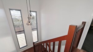 A wooden staircase with a railing leading to a landing with two windows. - 12th Tee Bed and Breakfast (Bargara)
