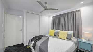 Een slaapkamer met een bed, een nachtkastje, een plafondventilator en een raam met gordijnen.