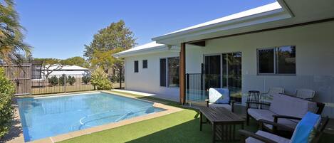 Una casa moderna con piscina, mobiliario de patio y una zona exterior cubierta.