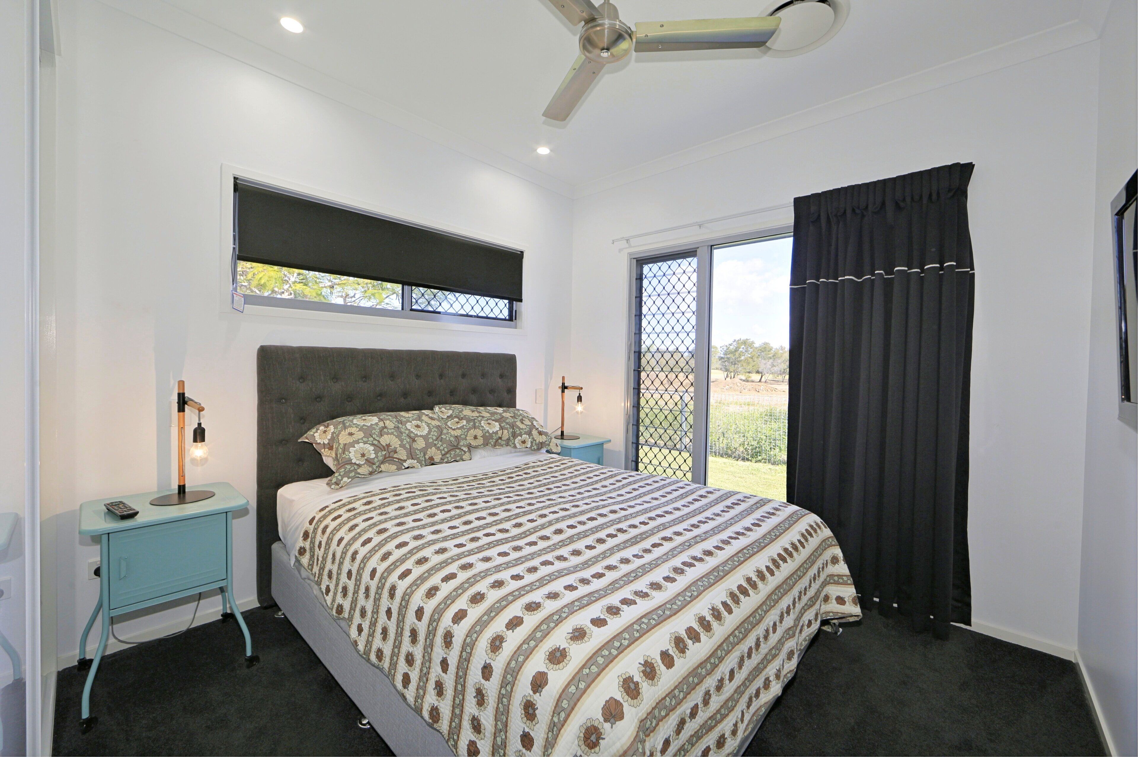 A bedroom with a bed, a nightstand, a ceiling fan, a window with a view, and a sliding door.