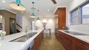 A modern kitchen with white countertops, wooden cabinets, and pendant lighting. - 12th Tee Bed and Breakfast (Bargara)