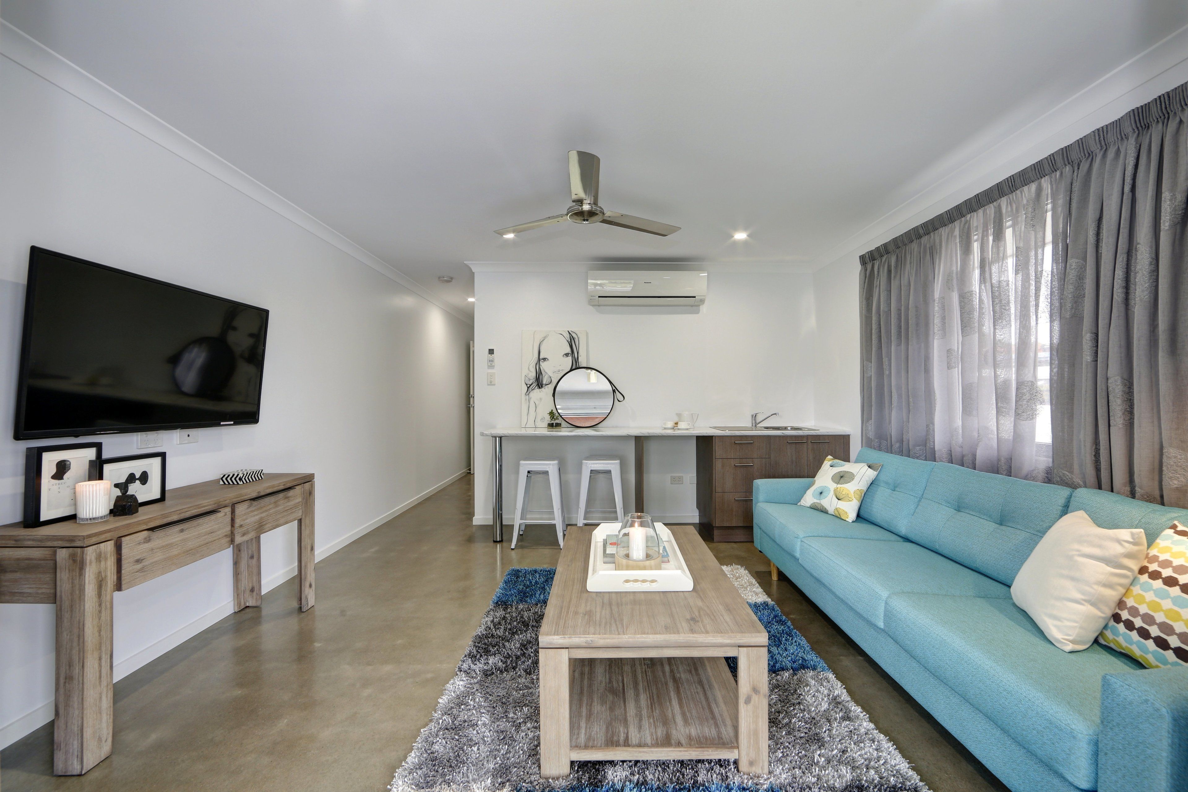 A modern living room with a blue sofa, wooden coffee table, and a flat-screen TV mounted on the wall.