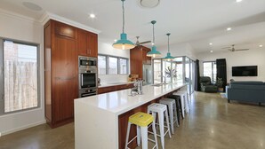 A modern kitchen with wooden cabinets, a white countertop, and bar stools. - 12th Tee Bed and Breakfast (Bargara)