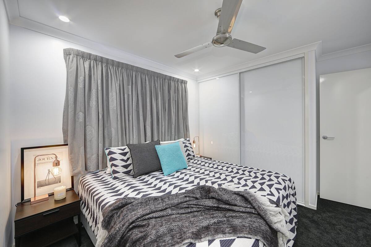 A bedroom with a bed, a nightstand, a framed picture, a ceiling fan, and a door.