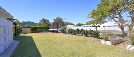 A well-maintained backyard with a lawn, a fenced area, and a variety of plants and trees.