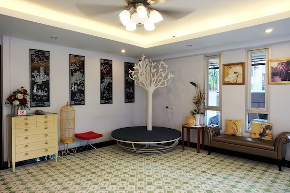 Una habitación con una plataforma redonda negra, un aparador amarillo, una silla roja, una mesa de madera con una planta y un sofá con cojines estampados.