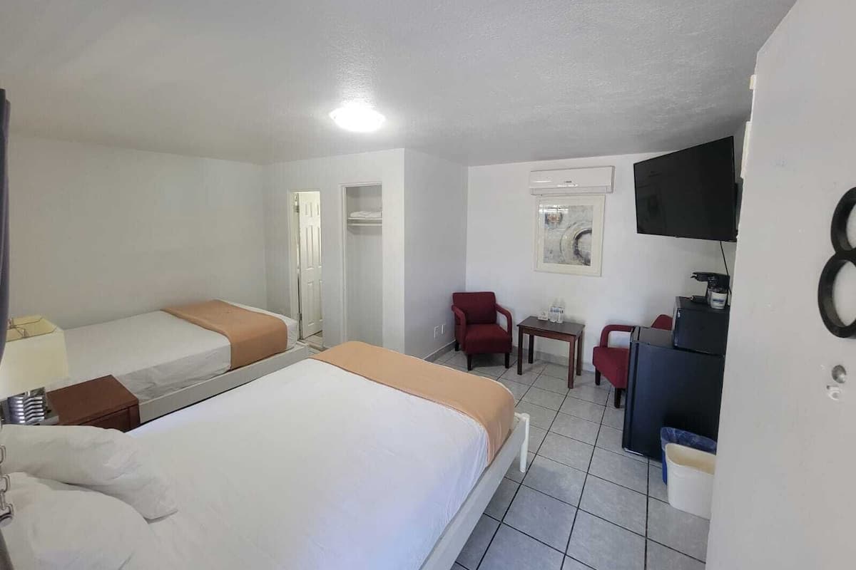 Habitación de hotel con dos camas individuales, un escritorio con silla, televisor montado en la pared y un armario.