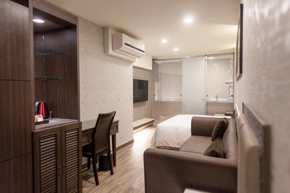 A modern hotel room with a wooden desk, a comfortable sofa, a bed, and a large mirror.
