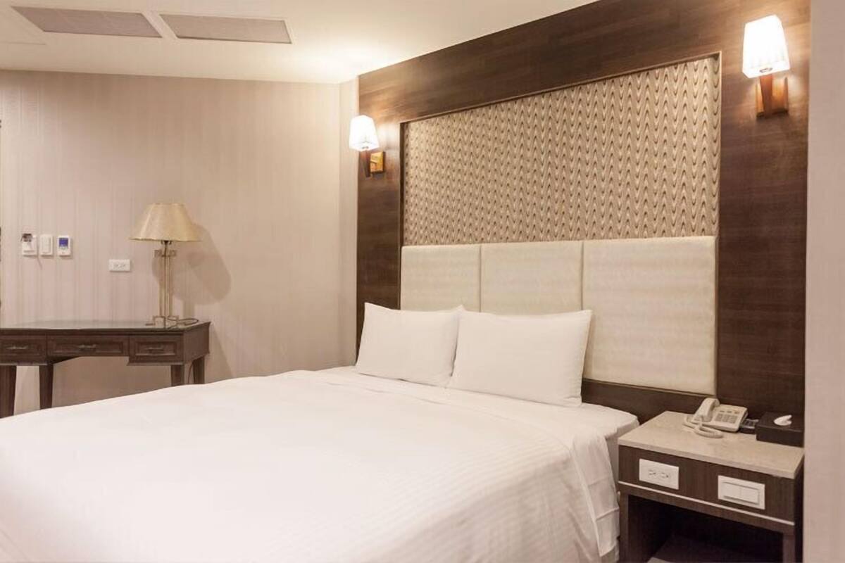 A hotel room with a large bed, a wooden headboard, bedside lamps, a desk, and a telephone.