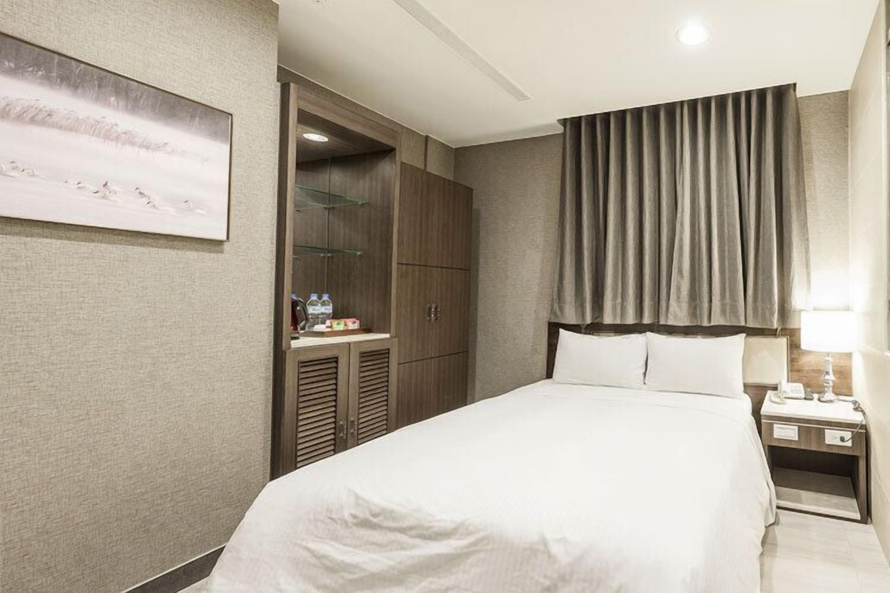 A hotel room with a large bed, a nightstand, a wardrobe, and a painting on the wall.