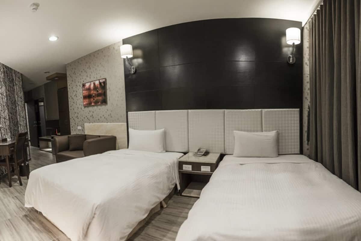 A hotel room with two beds, a desk, a chair, and a nightstand with a phone.