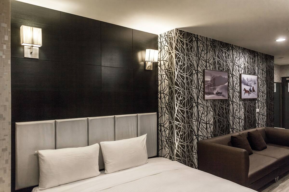 A modern hotel room with a large bed, a brown sofa, and a patterned wall.