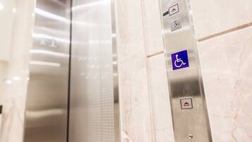 An elevator interior with a marble wall, a disabled access button, and a directional arrow button.