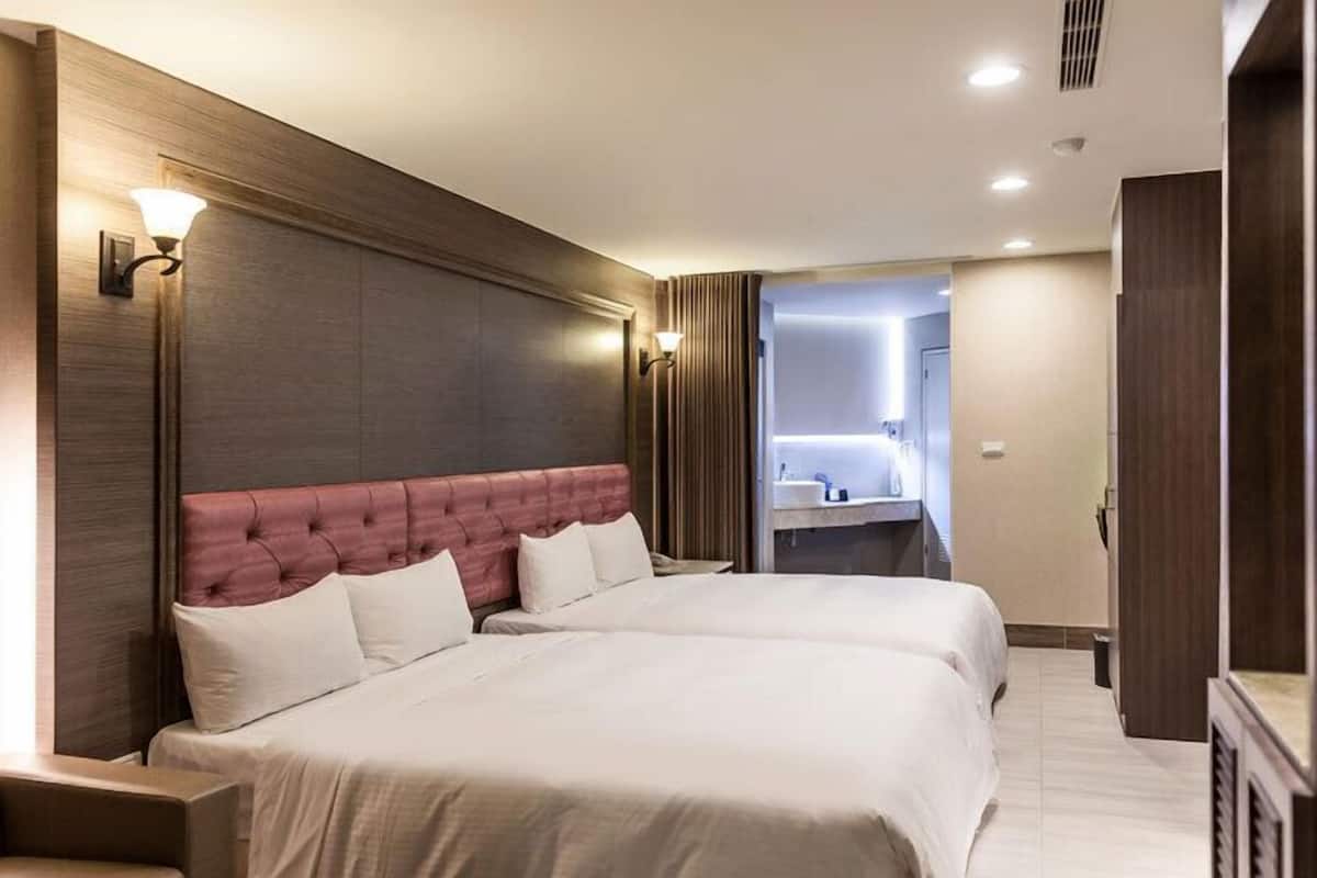 A hotel room with a large bed, two bedside tables, a headboard, and a bathroom visible through an open door.