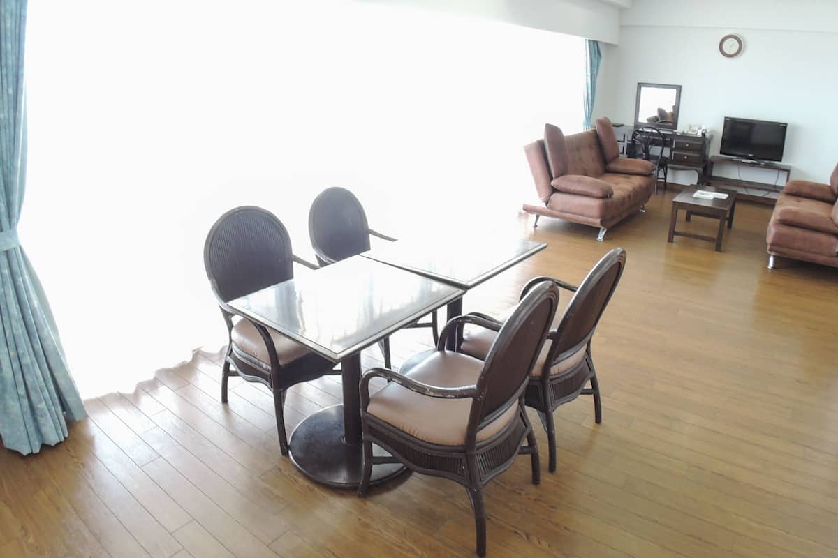 A modern living room with a dining area, featuring a glass table, wicker chairs, and a sofa set.
