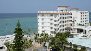 Un hotel de varios pisos con balcones con vistas al mar, rodeado de palmeras y un cielo despejado.