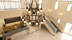 Vestíbulo de hotel con candelabro, mostrador de recepción, escalera y obras de arte en la pared.