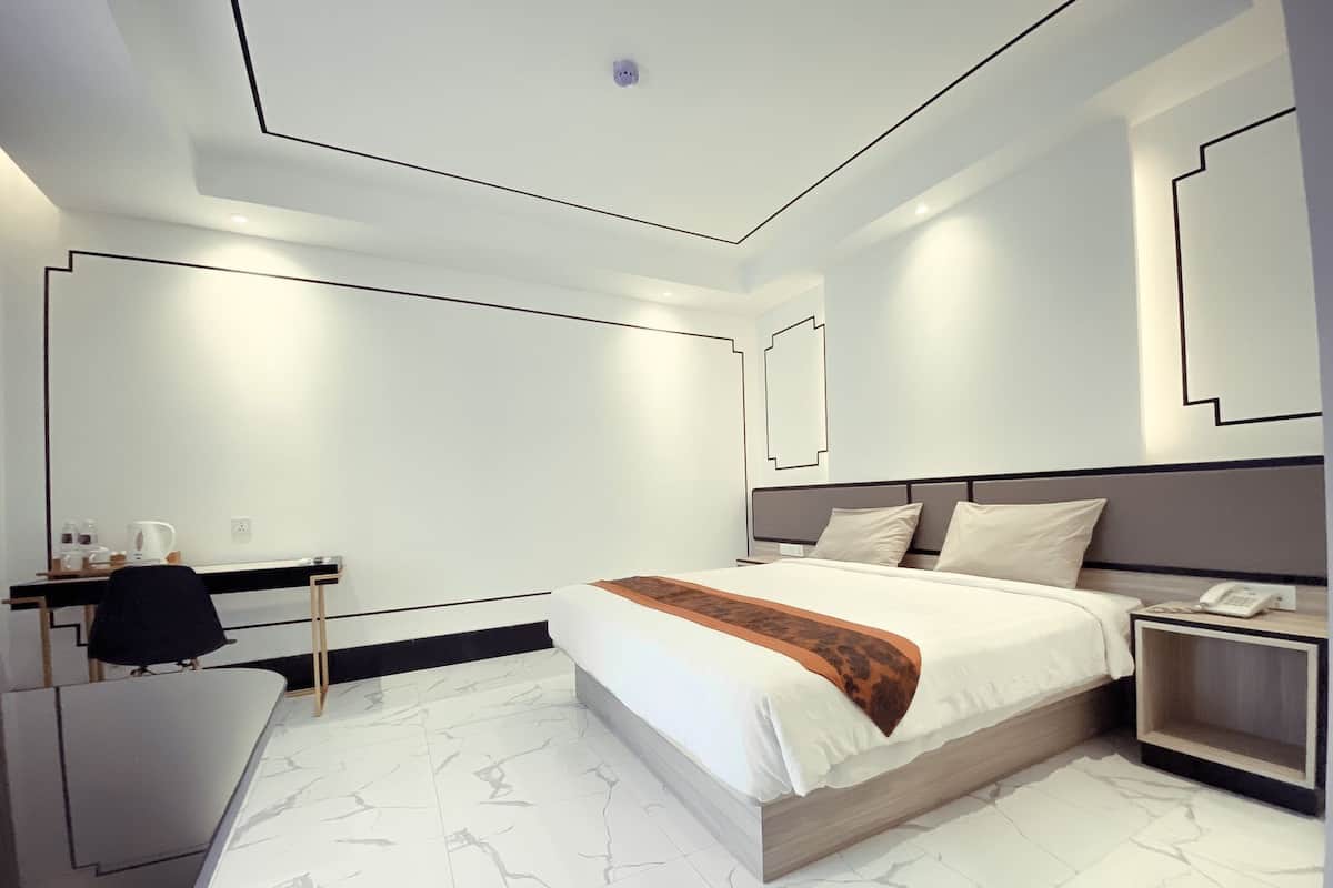 A modern hotel room with a bed, bedside table, desk, and chair.