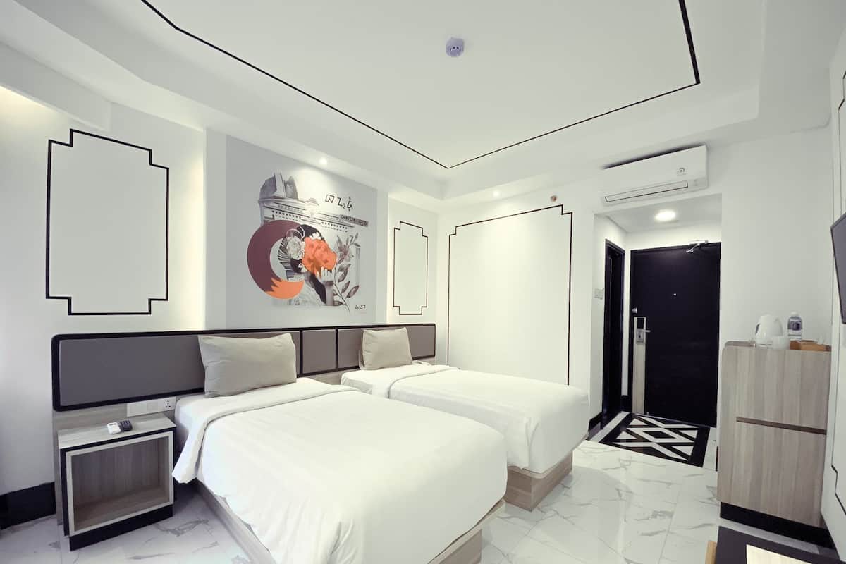A modern hotel room with two beds, a large mirror, a wall art piece, and a black and white patterned rug.