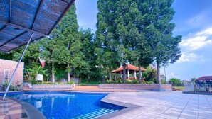 A swimming pool with a tiled deck, surrounded by trees and a gazebo. - De Ningrat Topas Galeria (Bandung)