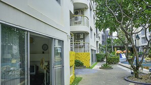 Un edificio residencial de varios pisos con balcones, un pequeño jardín y una entrada visible con puertas de vidrio.