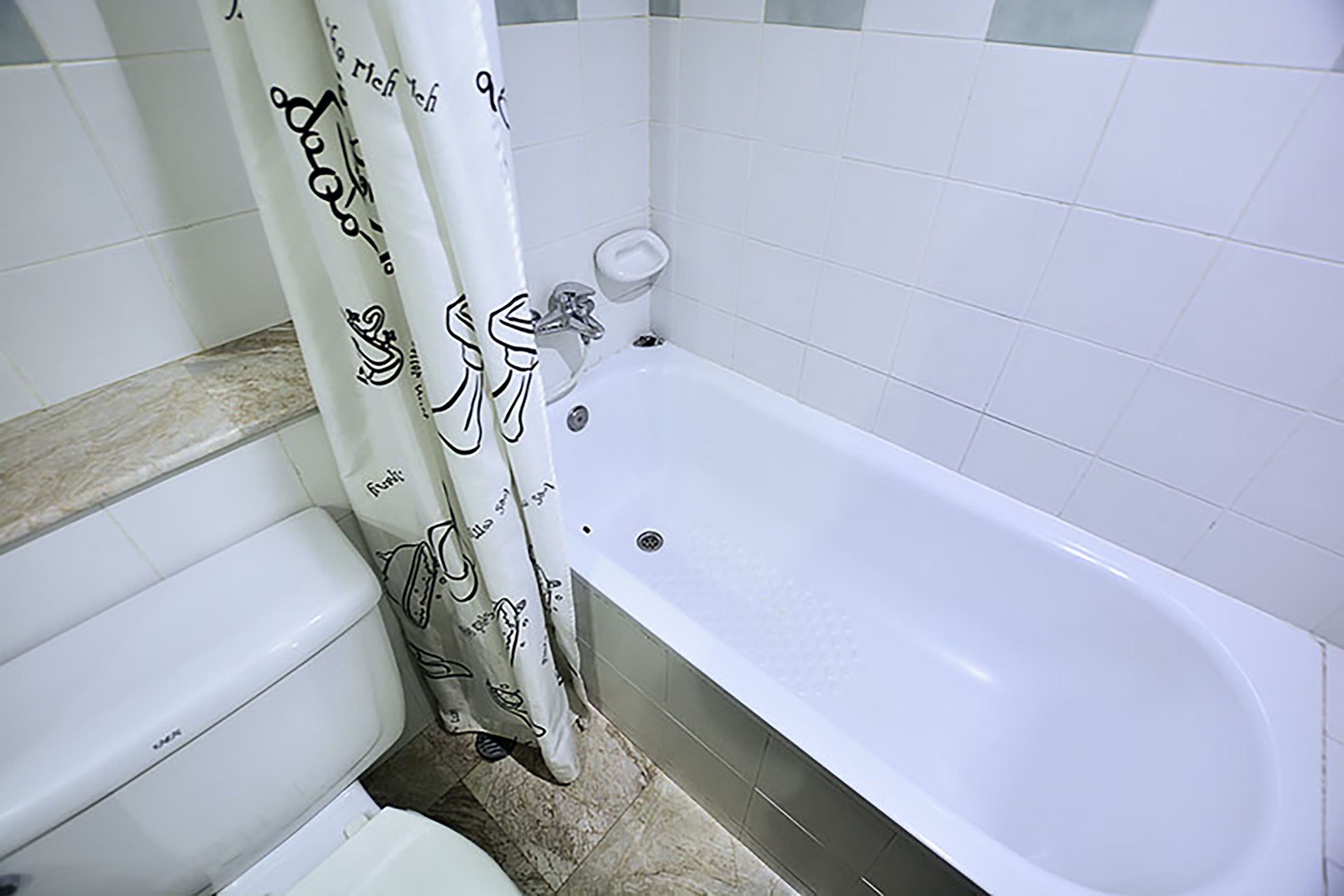 Un baño con bañera, inodoro y cortina de ducha decorada.