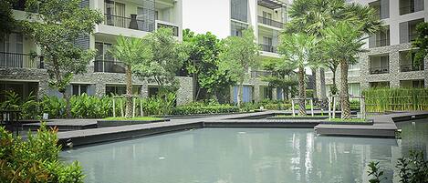 A modern hotel courtyard with a central pool, surrounded by multi-story buildings with balconies and lush greenery.