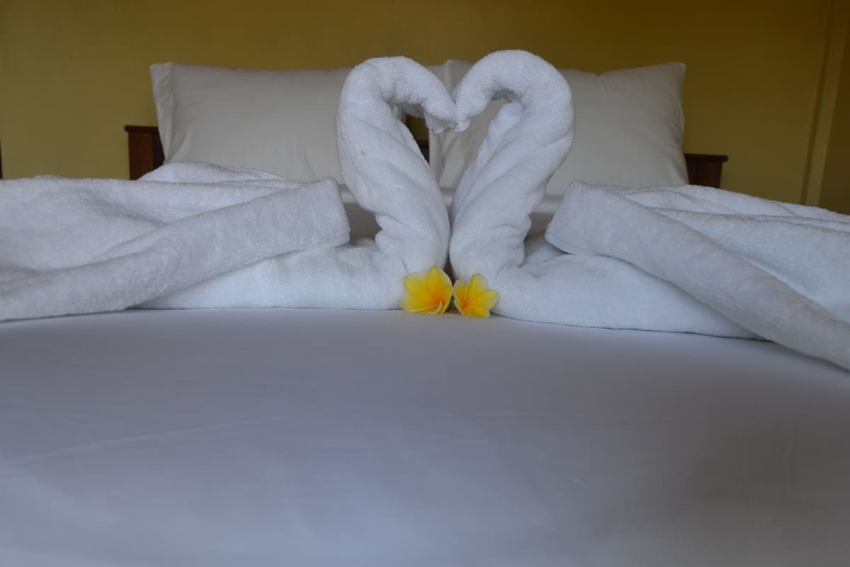 Una cama con sábanas blancas y dos flores amarillas al pie.