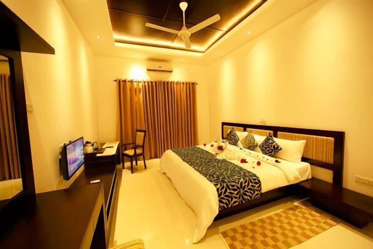 A hotel room with a bed, a desk, a chair, a television, and a ceiling fan.